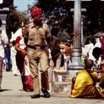 A bustling street scene in India featuring a diverse crowd and a policeman walking amidst people.