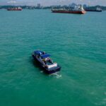 A lone boat navigates through a bustling shipping channel on a clear day.