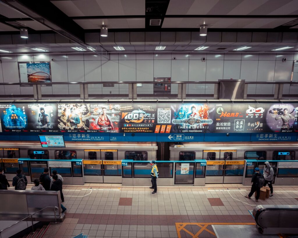 High angle view of a metro station with colorful advertisements and commuters standing and waiting.