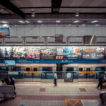 High angle view of a metro station with colorful advertisements and commuters standing and waiting.