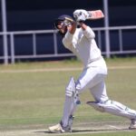 Cricketer in action hitting a shot on an outdoor field during a sunny day.