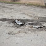 A fragment of a military shell lies on a rural road, depicting destruction.