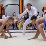Two young wrestlers engage in a traditional wrestling match indoors with an attentive audience.