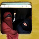 Women in burqas gazing outside a train window in Dhaka, Bangladesh, capturing cultural essence and travel mood.