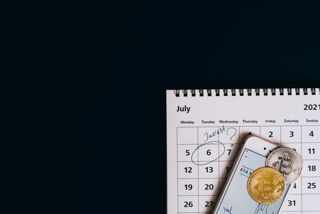 Top view of bitcoins and smartphone on July 2021 calendar, suggesting investment planning.