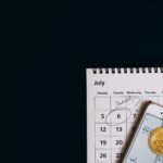Top view of bitcoins and smartphone on July 2021 calendar, suggesting investment planning.