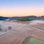 A scenic aerial view of misty farmland and rolling hills during sunrise in Urne, Wisconsin.