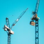 Two tower cranes dominate the skyline with a bright blue sky backdrop in Manchester.