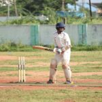 A cricketer in action on a sunny outdoor field in full gear, ready to bat.