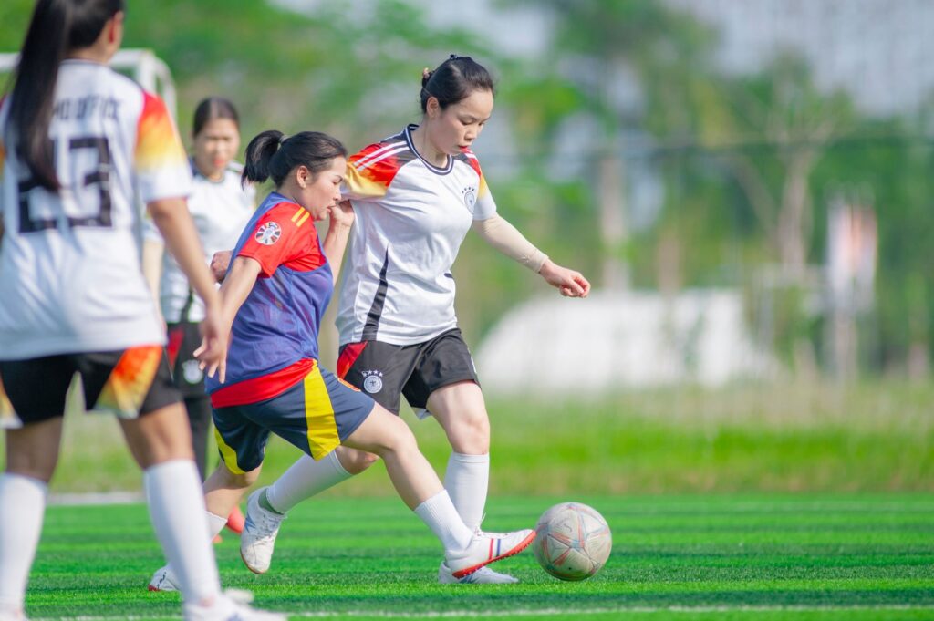 Women playing soccer on a vibrant green field in Hanoi, Vietnam. Team sports and outdoor activity.