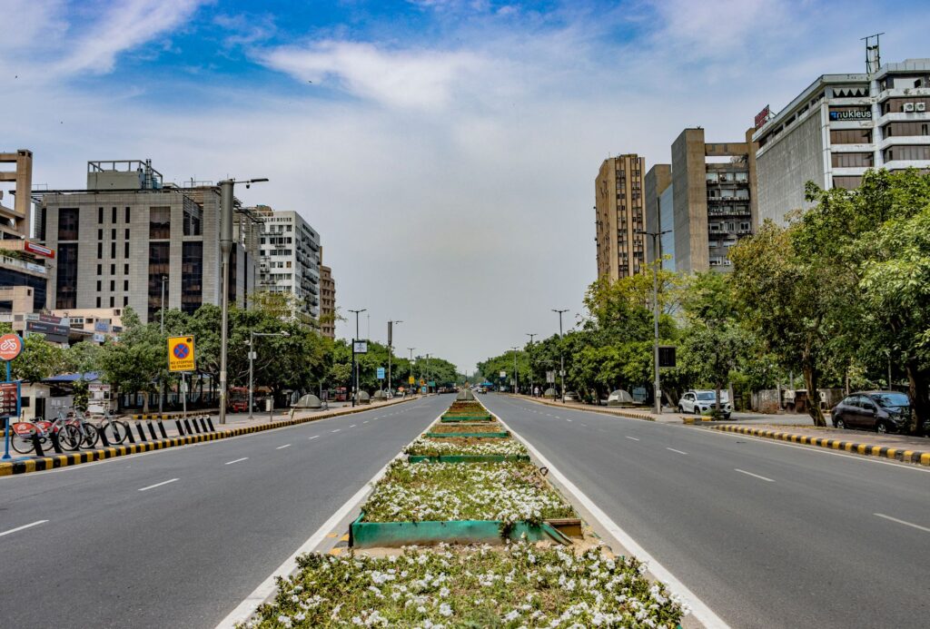 A vibrant urban scene in New Delhi, showcasing modern architecture and a wide, empty road.