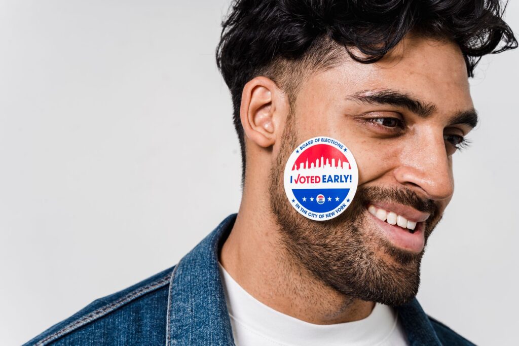 Smiling young man with 'I Voted Early' sticker on cheek, demonstrating civic participation.