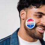 Smiling young man with 'I Voted Early' sticker on cheek, demonstrating civic participation.