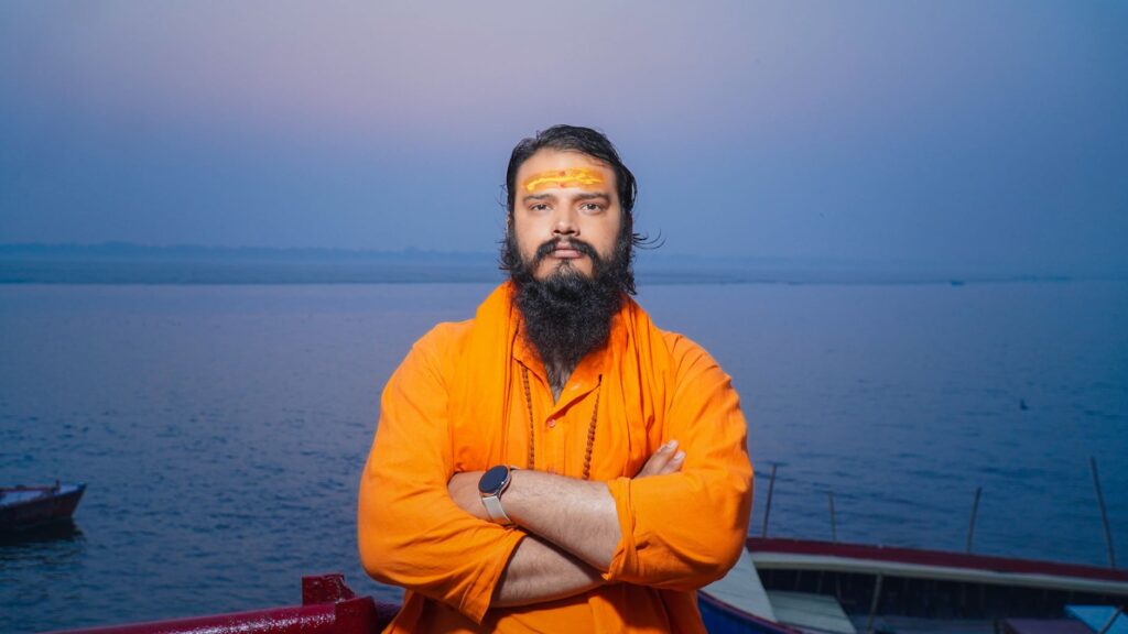 A spiritual Hindu sadhu stands confidently by the Ganges River in Varanasi, India, during twilight.
