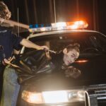 A police officer handcuffing a suspect on a patrol car at night.