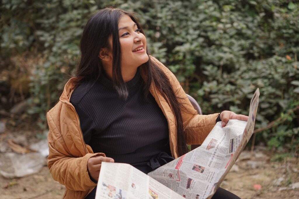Young woman reading a newspaper outdoors in Delhi, enjoying a sunny day.