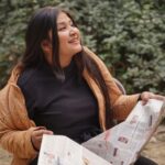 Young woman reading a newspaper outdoors in Delhi, enjoying a sunny day.