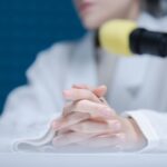 Close-up of hands folded near a microphone in a podcast studio.