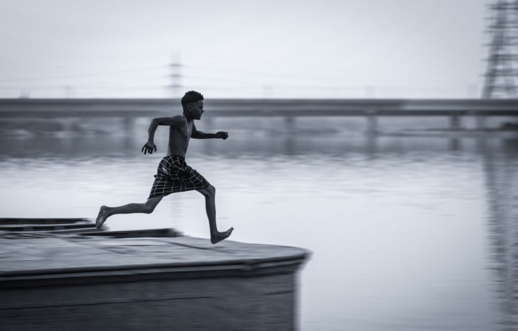 A young man in mid-air leaping over water, capturing the essence of freedom and dynamic movement.