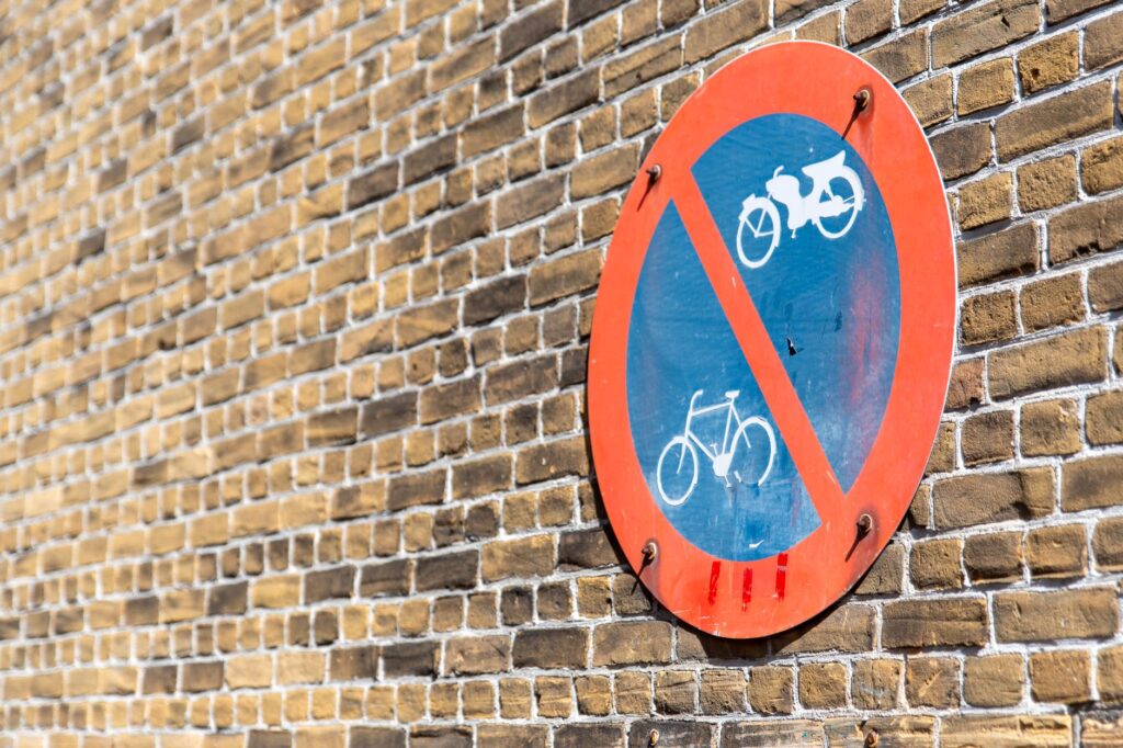 Traffic sign prohibiting cycling against a brick wall brightly lit by sunlight.