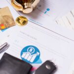 Close-up of financial documents, credit cards, coins, and a pen on a wooden desk.