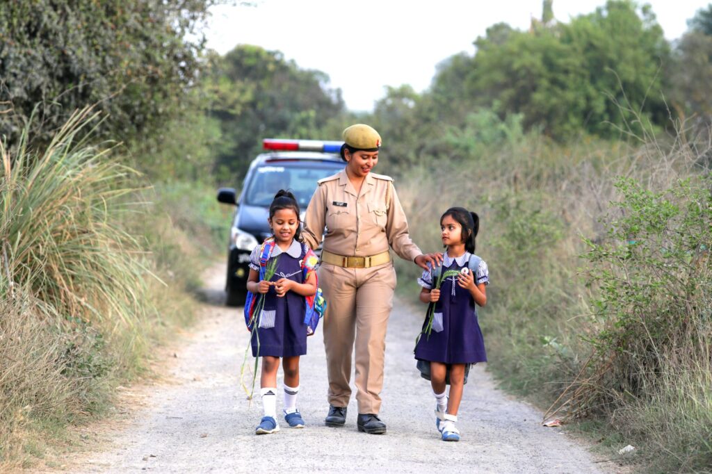 A caring police officer escorts two happy children walking on a rural road.