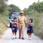 A caring police officer escorts two happy children walking on a rural road.
