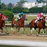 Jockeys racing horses energetically on a sunlit track during an exciting competition.