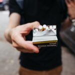 Close-up of a man offering a pack of cigarettes outdoors on a city street.