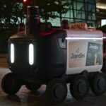 Close-up view of an autonomous delivery robot on a city street at night under artificial light.
