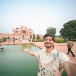 A traveler takes a selfie at Humayun's Tomb in Delhi, showcasing Mughal architecture and a beautiful garden.
