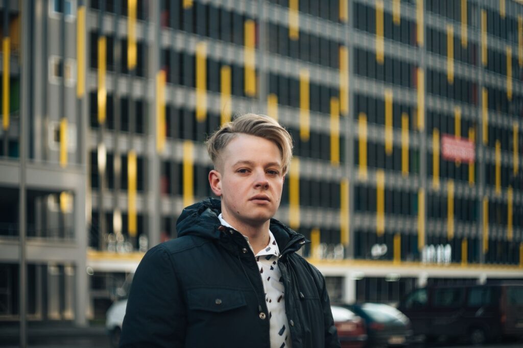Stylish man with blonde hair in urban setting, wearing a dark jacket.