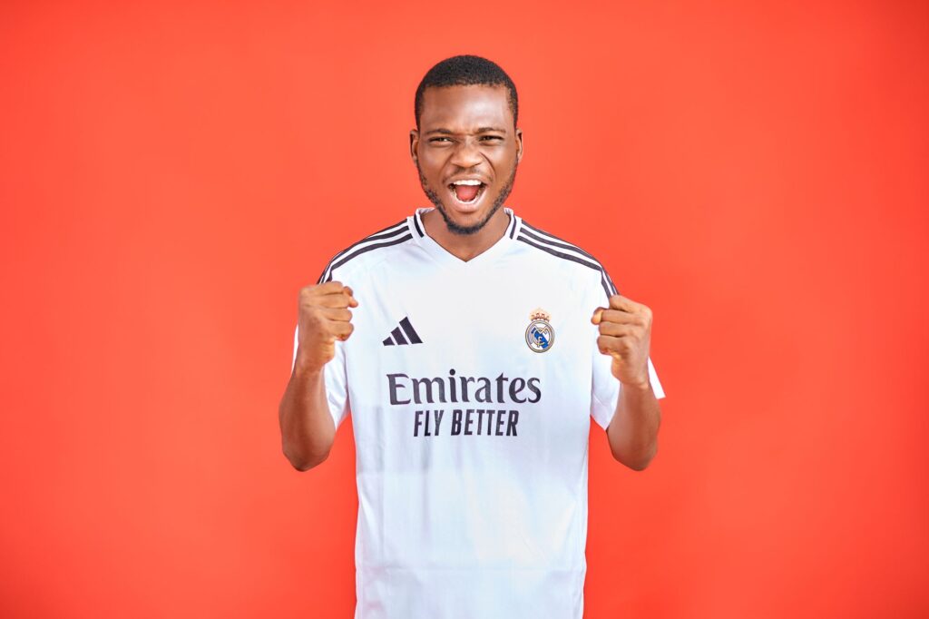 Energetic soccer fan in a team jersey cheering against a vibrant red background.