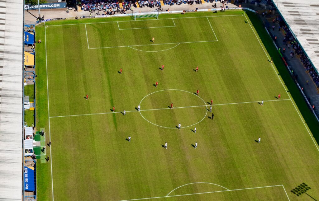 Aerial view of a football match in a sunlit stadium in Manchester.