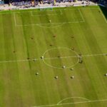 Aerial view of a football match in a sunlit stadium in Manchester.