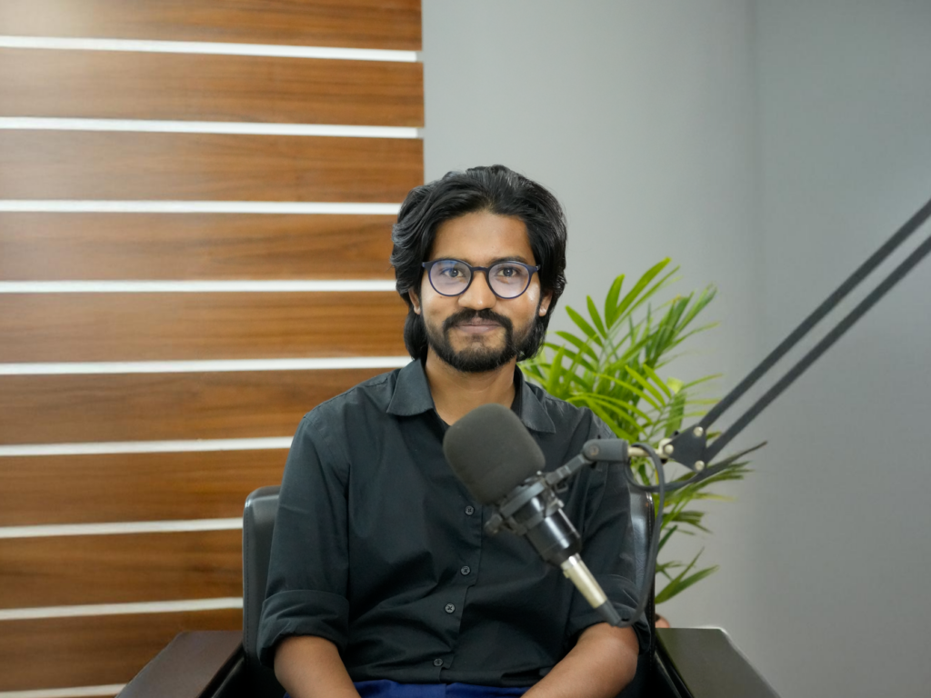 A confident South Asian man in a studio, ready for podcasting with a professional microphone setup.