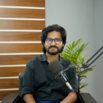 A confident South Asian man in a studio, ready for podcasting with a professional microphone setup.