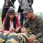 A group of people providing first aid to an injured soldier in an outdoor setting.