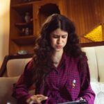A woman sitting indoors looking frustrated with a tablet in hand, wearing pajamas.