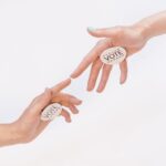 Two hands reaching with vote stickers, symbolizing participation and democracy in elections.