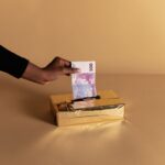 Euro banknote held by a hand against beige background, symbolizing bribery or gifting.