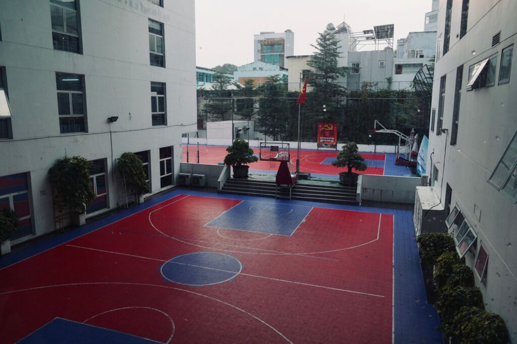 Aerial view of an urban school basketball court, surrounded by buildings.