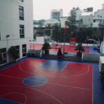 Aerial view of an urban school basketball court, surrounded by buildings.