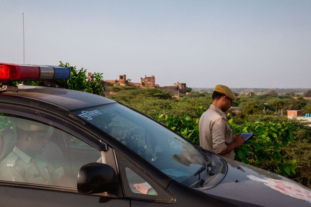 Police officer using tablet beside patrol car in scenic outdoor setting.