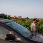 Police officer using tablet beside patrol car in scenic outdoor setting.