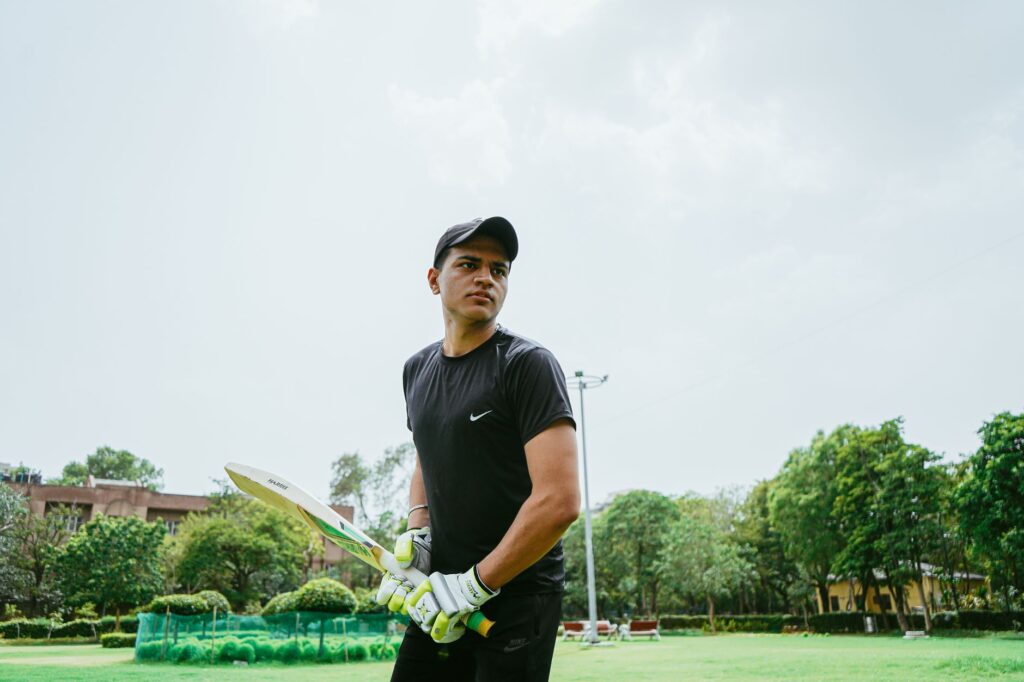 Ethnic sportsman wearing sportswear and cricket gloves preparing for hitting ball while standing on field and looking away