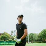 Ethnic sportsman wearing sportswear and cricket gloves preparing for hitting ball while standing on field and looking away