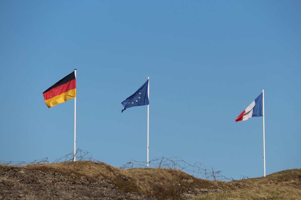 Flags of Germany, European Union, and France flying outdoors against a clear sky.