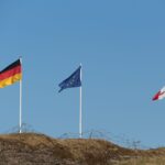 Flags of Germany, European Union, and France flying outdoors against a clear sky.