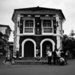 Monochrome image of a vintage colonial building with people in an urban setting.